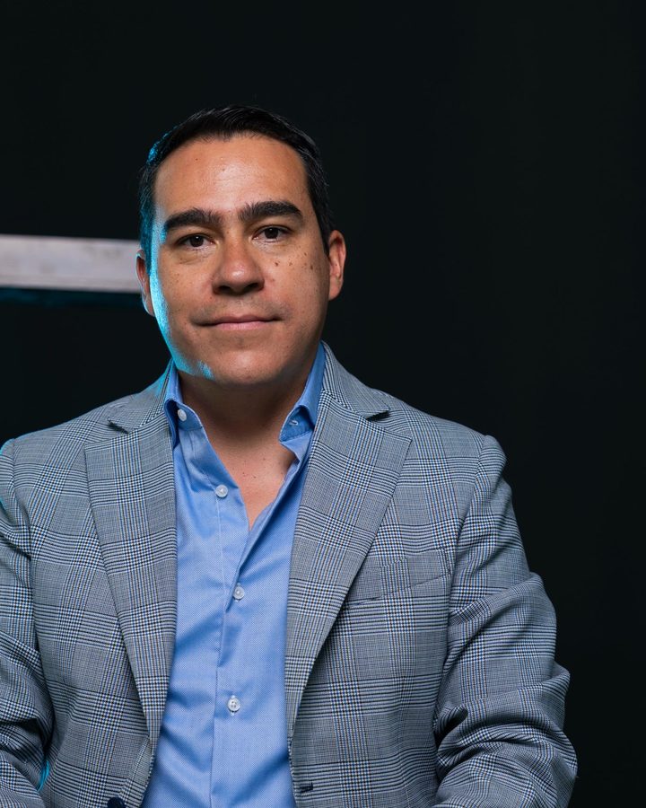 Alejandro Robles, director de FURO Capital, sentado de frente con saco gris a cuadros sobre fondo negro.