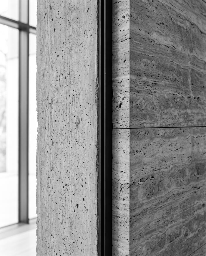 Detalle monocromático de concreto aparente junto a un muro de travertino.